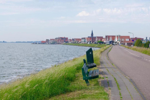 Carretera costera con bancos verdes junto al agua y vista panorámica de Volendam, Países Bajos.