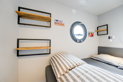 Cabina moderna sulla houseboat 'La Belle Vie' nei Paesi Bassi, con letto a righe e oblò tondo.