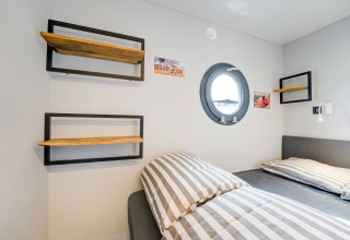 Cabina moderna sulla houseboat 'La Belle Vie' nei Paesi Bassi, con letto a righe e oblò tondo.