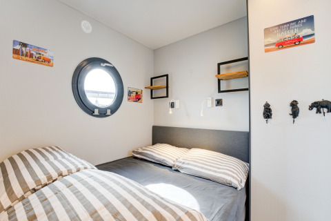 Camera accogliente con biancheria a righe, oblò rotondo e decorazioni sul muro sulla houseboat La Belle Vie.