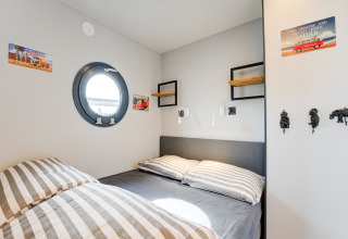 Camera accogliente con biancheria a righe, oblò rotondo e decorazioni sul muro sulla houseboat La Belle Vie.