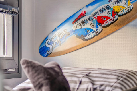 Surfplank met vrolijke busjes en 'gone Surfing' als wanddecoratie in een slaapkamer van een woonboot.