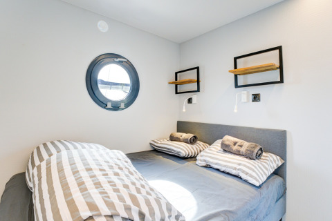 Camera da letto con letto matrimoniale, lenzuola a righe e oblò sulla houseboat 'La Belle Vie' nei Paesi Bassi.
