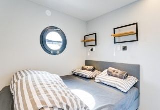 Camera da letto con letto matrimoniale, lenzuola a righe e oblò sulla houseboat 'La Belle Vie' nei Paesi Bassi.