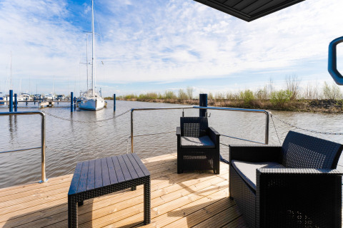 Vista dal houseboat 'La Belle Vie' nei Paesi Bassi con sedie e barche a vela ormeggiate sullo sfondo.