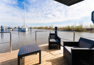 Vista dal houseboat 'La Belle Vie' nei Paesi Bassi con sedie e barche a vela ormeggiate sullo sfondo.
