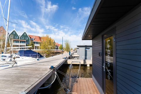 Houseboat 'La Belle Vie' ormeggiato in un porto olandese, vicino a barche e case tradizionali.