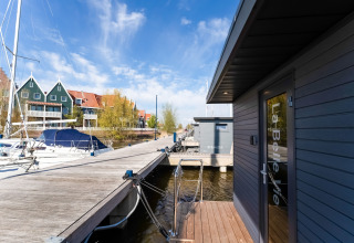 Houseboat 'La Belle Vie' ormeggiato in un porto olandese, vicino a barche e case tradizionali.