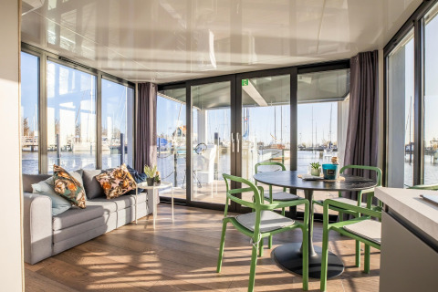 Lyst og moderne opholdsområde med sofa og spisebord på husbåden Marina Sunrise i Holland, udsigt til marina.
