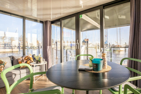 Lys stue på husbåd Marina Sunrise i Holland med udsigt over marinaen gennem store vinduer.