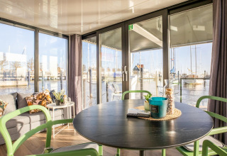 Lys stue på husbåd Marina Sunrise i Holland med udsigt over marinaen gennem store vinduer.