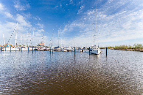 Marina con barche a vela ormeggiate vista dalla casa galleggiante La Belle Vie nei Paesi Bassi con cielo azzurro.