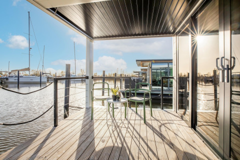Solrig terrasse på husbåd “Marina Sunrise” i Holland med udsigt over marinaen og moderne stole.