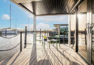 Solrig terrasse på husbåd “Marina Sunrise” i Holland med udsigt over marinaen og moderne stole.