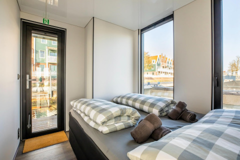 Moderne soveværelseinteriør på husbåd 'Marina Sunrise' med store vinduer i Holland, udsigt til vandet.
