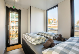 Moderne soveværelseinteriør på husbåd 'Marina Sunrise' med store vinduer i Holland, udsigt til vandet.