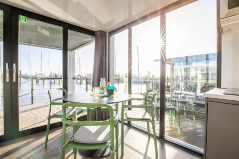Spisestue med store vinduer på husbåden «Marina Sunrise» i Holland med udsigt til lystbådehavn.