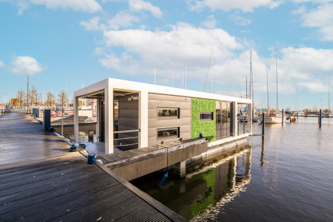 Moderne husbåd 'Marina Sunrise' fortøjet ved en marina i Holland under en blå himmel.