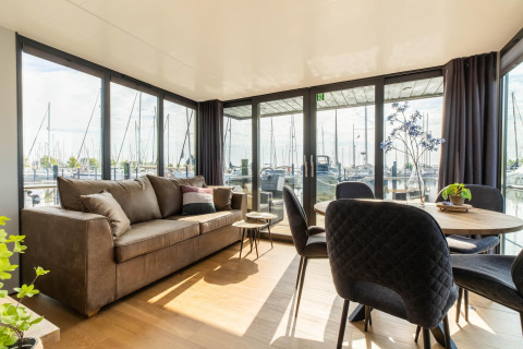 Salon lumineux d’une péniche à Volendam Marina, Pays-Bas, avec de grandes fenêtres et vue sur le port.