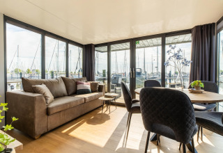 Sala luminosa en una casa flotante en Volendam Marina, Países Bajos, con vistas al puerto y amplios ventanales.