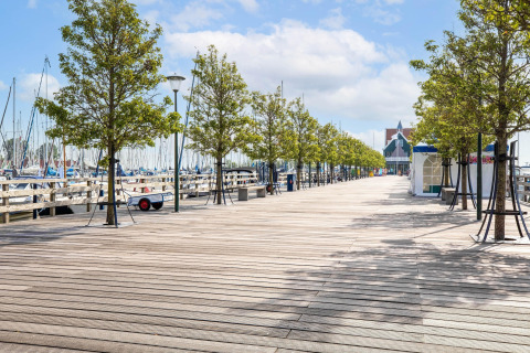 Paseo marítimo de madera con árboles y barcos en Volendam Marina, Países Bajos, en un día soleado.