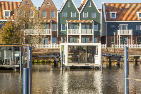 Hus med orange tage og en husbåd 'Marina Sunrise' fortøjet foran i Holland, klart dagslys.