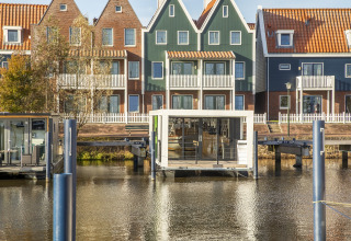Hus med orange tage og en husbåd 'Marina Sunrise' fortøjet foran i Holland, klart dagslys.