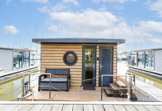 Hausboot in der Volendam Marina in den Niederlanden mit Holzfassade, Bank und Wasserblick.