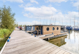 Péniche moderne amarrée à Volendam Marina, Pays-Bas, en bois clair, sur eau calme près d'un ponton.