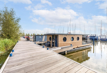 Péniche moderne amarrée à Volendam Marina, Pays-Bas, en bois clair, sur eau calme près d'un ponton.