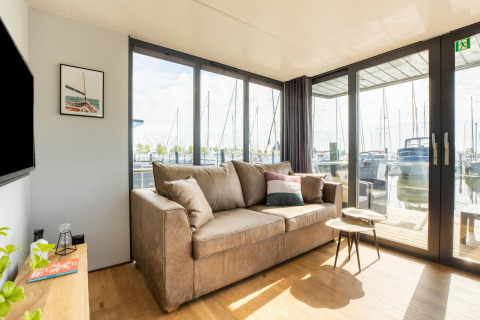 Lys stue på en husbåd i Volendam Marina, Holland, med sofa, borde og udsigt over lystbådehavnen.