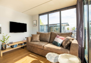 Stue med stor brun sofa, fladskærms-tv, og store vinduer på husbåd i Volendam Marina, Holland.