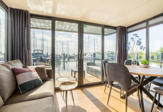 Lyst og moderne stue på husbåd med udsigt over Volendam Marina og sejlbåde i Holland.