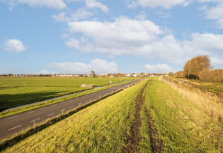 Udsigt fra husbåd 'Marina Sunrise' i Holland med en vej, grøn mark, vindmølle og blå himmel.
