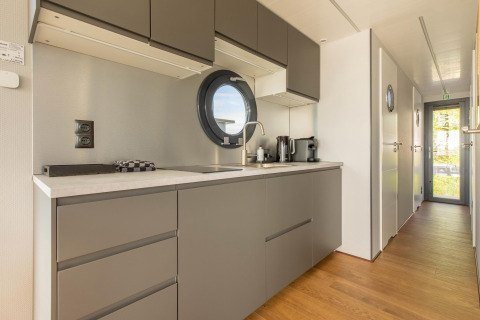Moderne keuken op een woonboot in Volendam Marina, Nederland, met ronde vensters en grijze kasten.