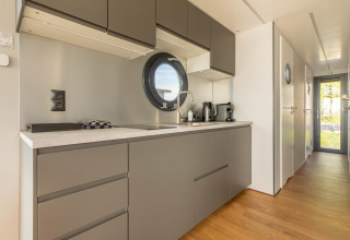 Modernes Hausboot-Küche in der Volendam Marina, Niederlande, mit runden Fenstern und grauen Schränken.