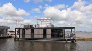 Houseboat moderno chiamato Houseboat Kohlenpott ormeggiato in porto con un cielo nuvoloso.
