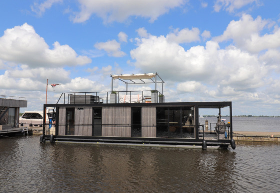 Modernes Hausboot namens Houseboat Kohlenpott liegt am Hafen unter bewölktem Himmel vor Anker.