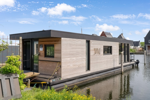 Moderne woonboot Boat House Stavoren aangemeerd aan een rustig kanaal, omringd door huizen.