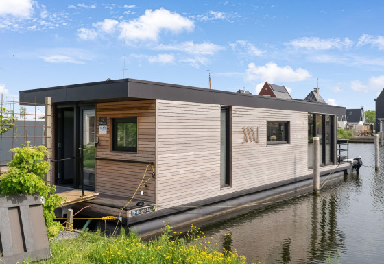 Moderne woonboot Boat House Stavoren aangemeerd aan een rustig kanaal, omringd door huizen.