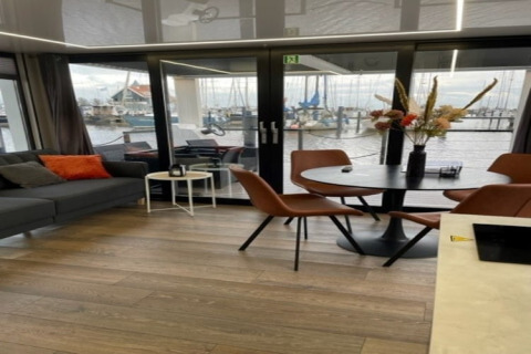 Moderne stue og spiseområde på husbåden 'Marina Sunrise' ved marinaen i Holland med udsigt til både.