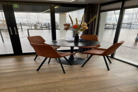 Moderne spiseplads på husbåd 'Marina Sunrise' i Holland med udsigt over vand og bådehavn gennem store vinduer.