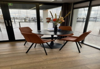 Moderne spiseplads på husbåd 'Marina Sunrise' i Holland med udsigt over vand og bådehavn gennem store vinduer.