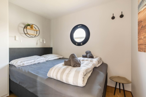 Modernes Schlafzimmer auf einem Hausboot in der Volendam Marina mit Bullaugenfenster und gemütlichem Bett.