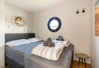 Modernes Schlafzimmer auf einem Hausboot in der Volendam Marina mit Bullaugenfenster und gemütlichem Bett.