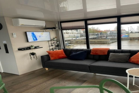 Moderne stue på husbåd 'Marina Sunrise' i Holland med sofa, farverige puder og udsigt over havnen.