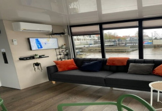 Moderne stue på husbåd 'Marina Sunrise' i Holland med sofa, farverige puder og udsigt over havnen.