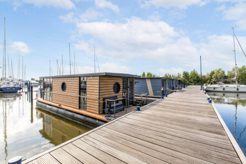 Ein modernes Hausboot an einem Holzsteg in der Volendam Marina, Niederlande, umgeben von Segelbooten.