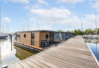 Una moderna houseboat ormeggiata a un molo di legno a Volendam Marina, nei Paesi Bassi, tra le barche a vela.