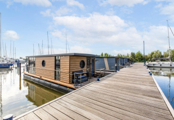 Une péniche moderne amarrée à un quai en bois à la marina de Volendam, aux Pays-Bas, près de voiliers.